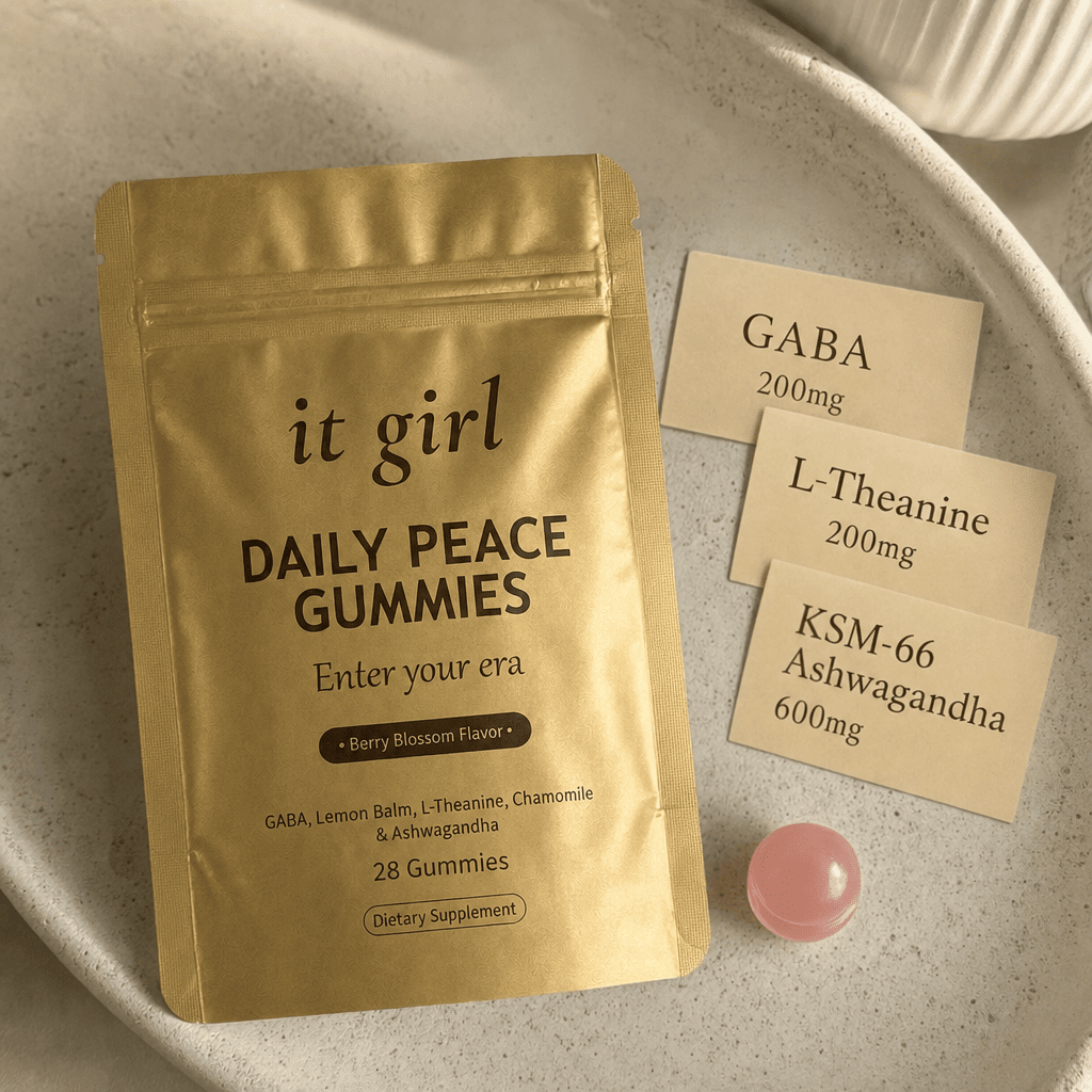 The real matte gold It Girl Daily Peace pouch on warm cream beside three dose cards reading GABA 200mg, L-Theanine 200mg, and KSM-66 Ashwagandha 600mg and a single pink gummy, the formula that hands the calm signal back directly