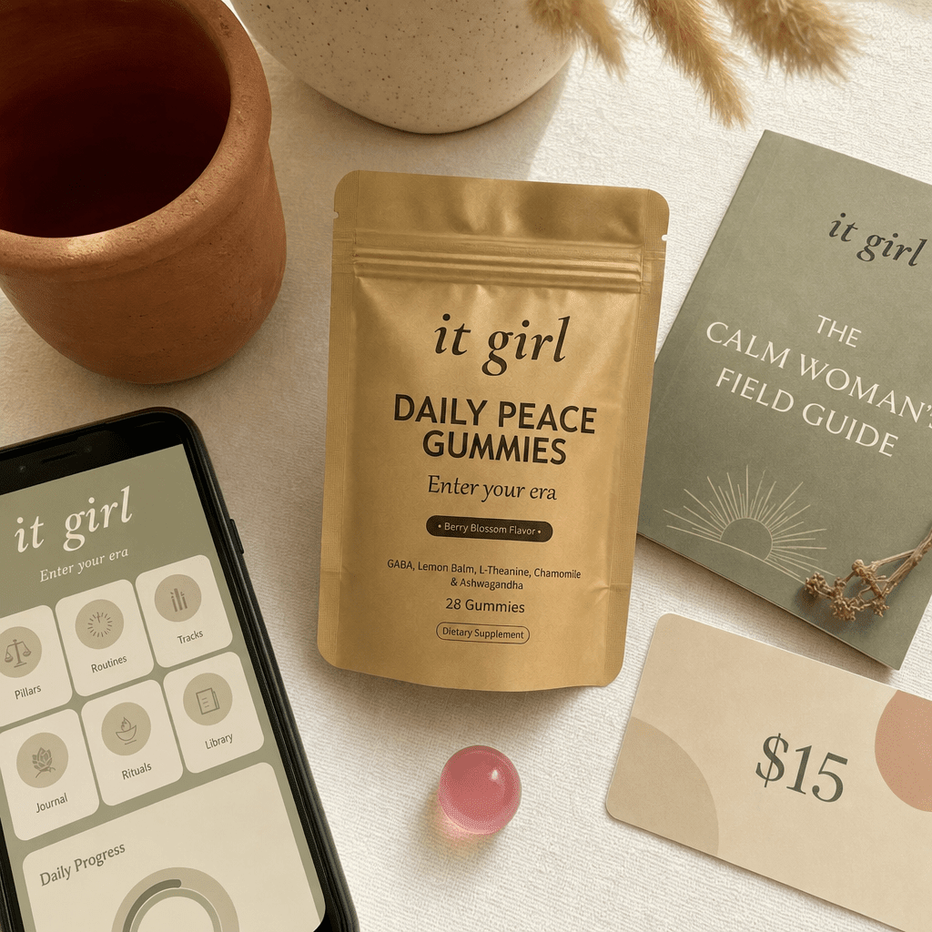 The real It Girl Daily Peace bundle on warm cream, the gold pouch front and center with the It Girl app on a phone, the Calm Woman's Field Guide booklet and a fifteen-dollar gift card, a whole month of calm for about a dollar a day