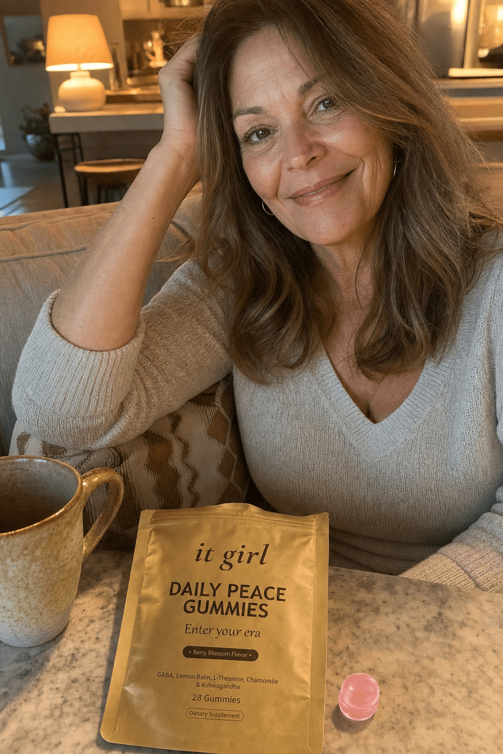 Warm candid evening photo of a relaxed woman in her fifties winding down at home, the real matte-gold It Girl Daily Peace pouch resting on the counter beside her, no wine glass
