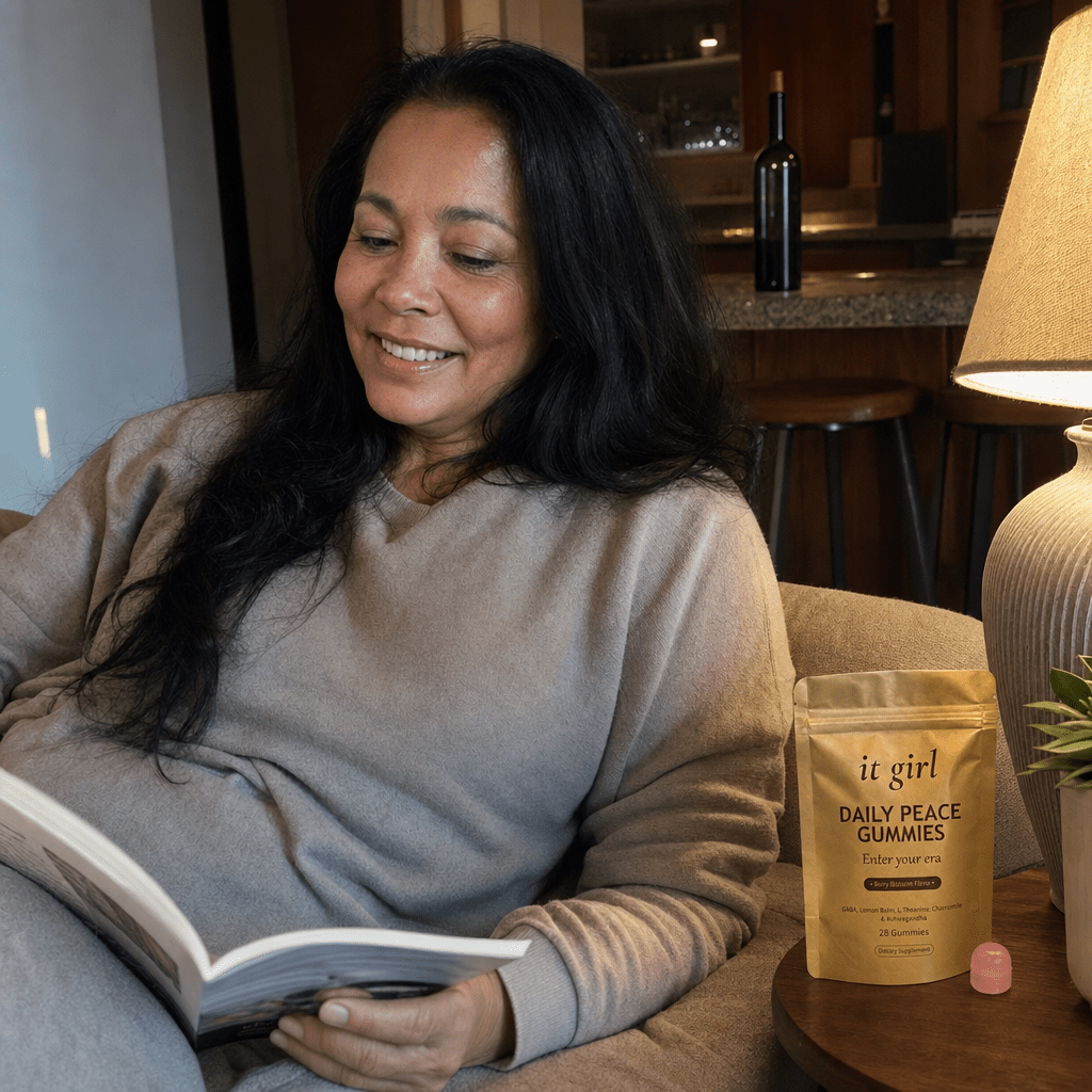 Warm documentary photo of a woman in her fifties relaxed on her couch in the evening, calm and unbothered, the real It Girl Daily Peace pouch on the side table and a forgotten corked wine bottle soft in the background