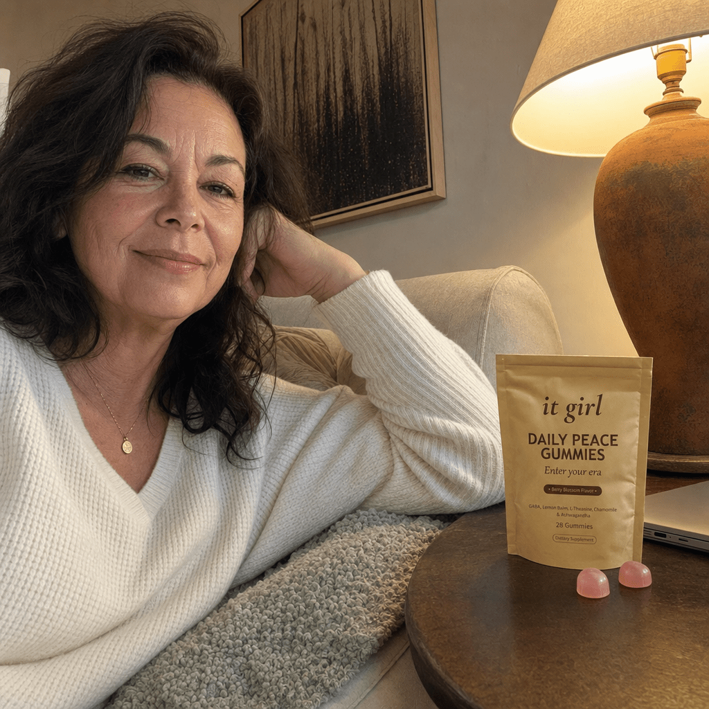 Real woman in her late fifties relaxed on her couch in the evening with the laptop closed, the gold It Girl Daily Peace pouch and a few gummies on the side table, the day finally letting go