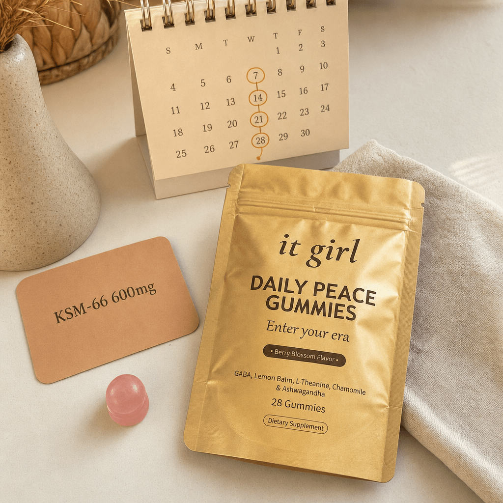 The real It Girl Daily Peace pouch beside a KSM-66 600mg dose card and a small month calendar, warm cream palette, the cortisol layer easing over four weeks
