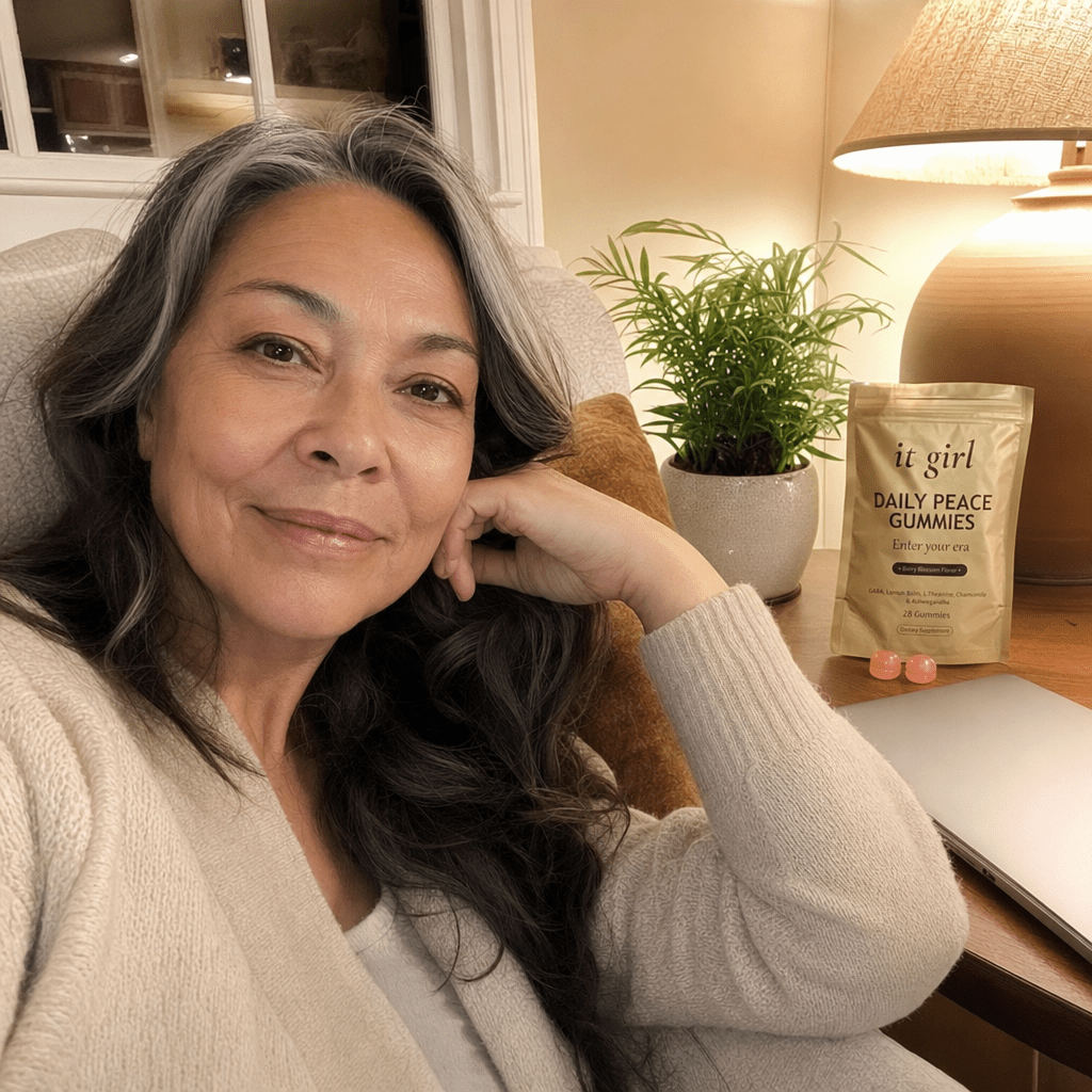 Real woman in her late fifties relaxed on her couch in the evening with the laptop closed, the gold It Girl Daily Peace pouch and a few gummies on the side table, the day finally letting go