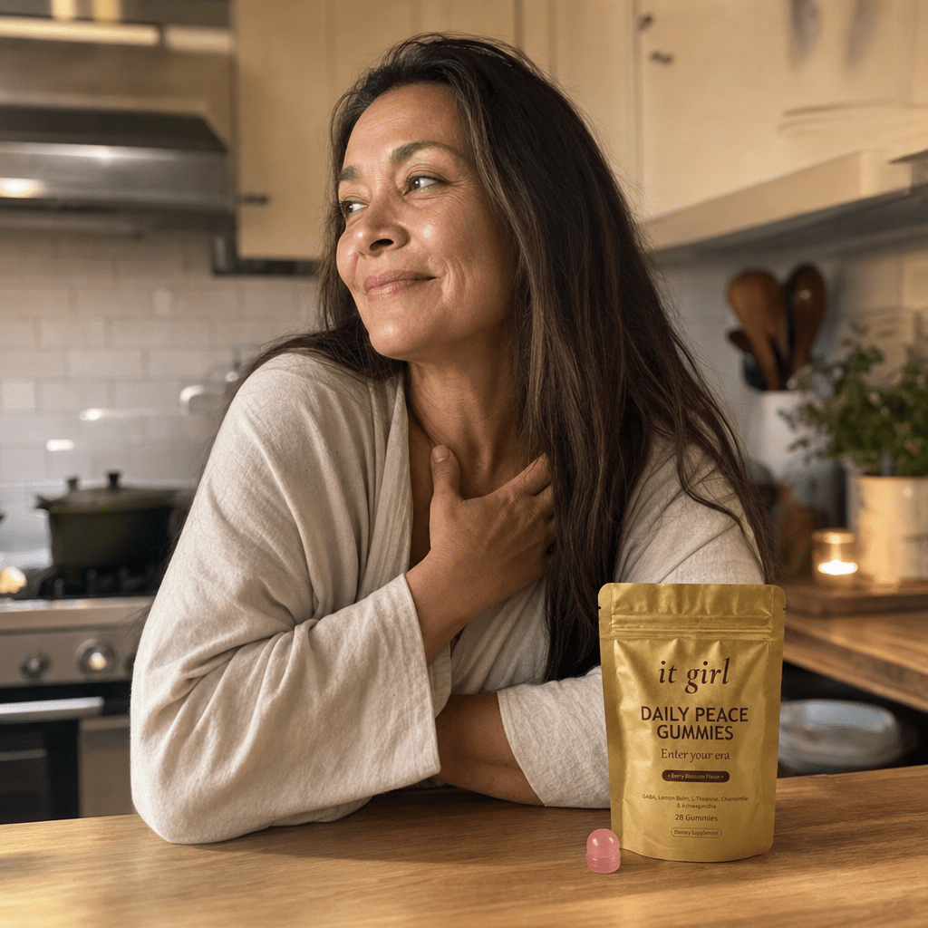 Real woman in her late fifties at ease in a warm-lit evening kitchen, calm and self-forgiving, the gold It Girl Daily Peace pouch resting on the counter, the reach finally understood and no risk in trying