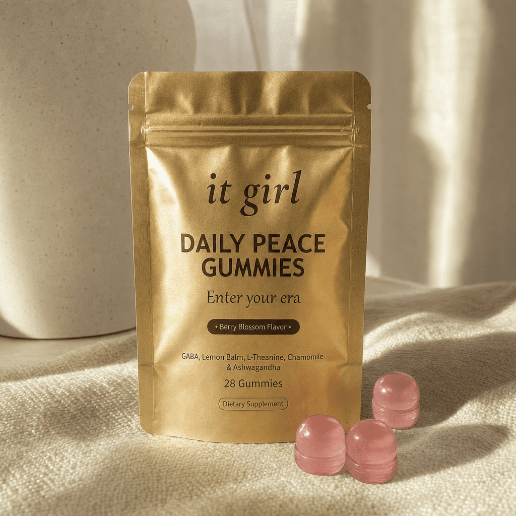 The gold It Girl Daily Peace pouch standing on a cream surface in warm morning light beside its gummies, the studied KSM-66 dose working on cortisol underneath