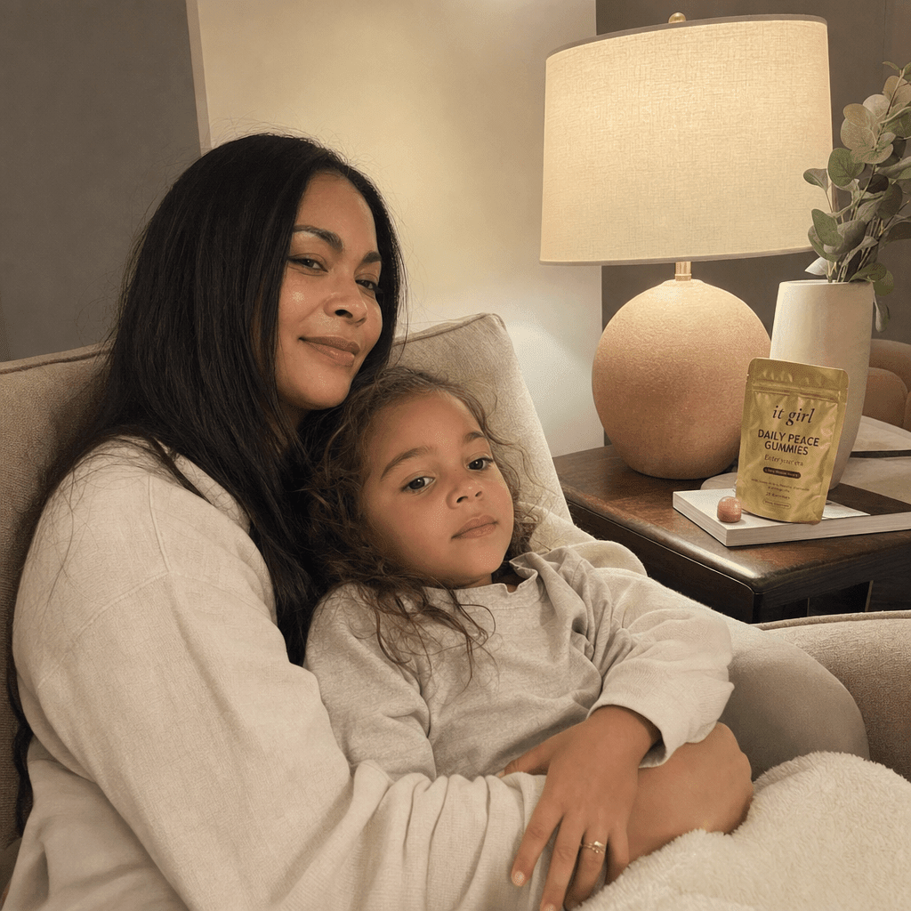 A present mother on the couch in warm lamplight with her child climbed back into her lap, the gold Daily Peace pouch resting in view on the side table