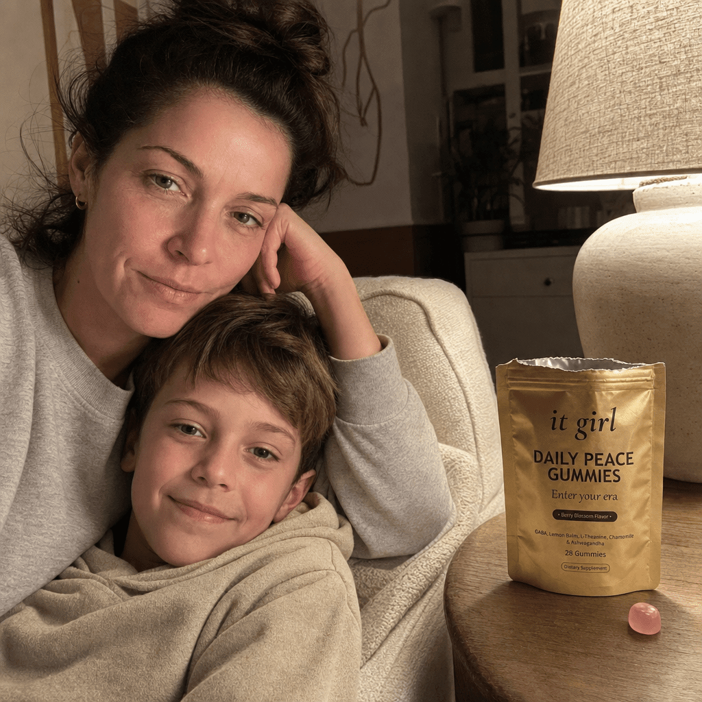 Restored calm mother on the couch with her young son climbing into her lap and staying, the real palm-sized gold It Girl Daily Peace pouch torn open with a loose pink gummy on the side table