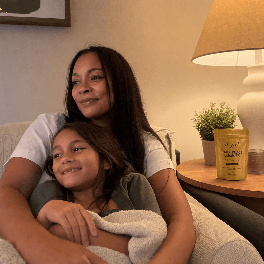 A present mother on the couch in warm lamplight with her nine-year-old climbed into her lap, her phone nowhere in sight, the gold Daily Peace pouch resting on the side table