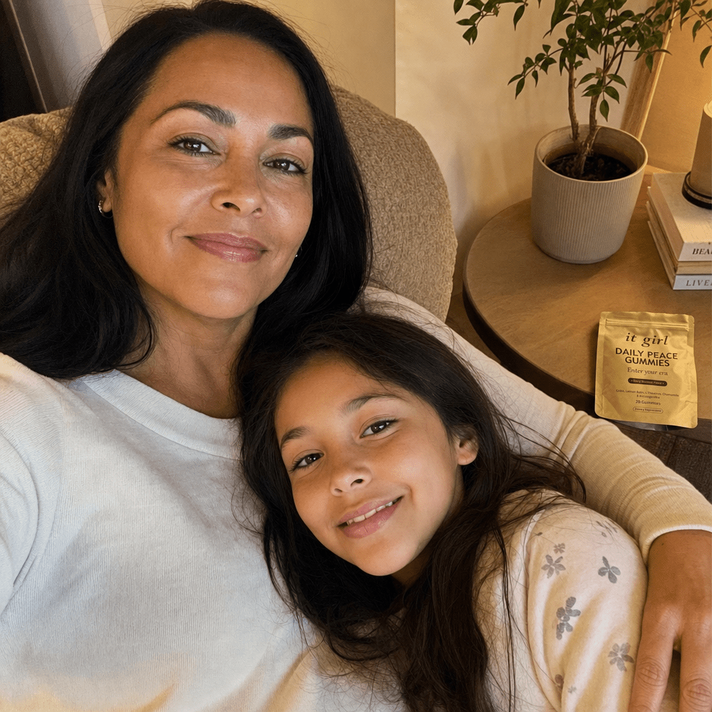 A rested woman in early-evening light with her young child leaning into her lap, the opened It Girl pouch resting nearby.