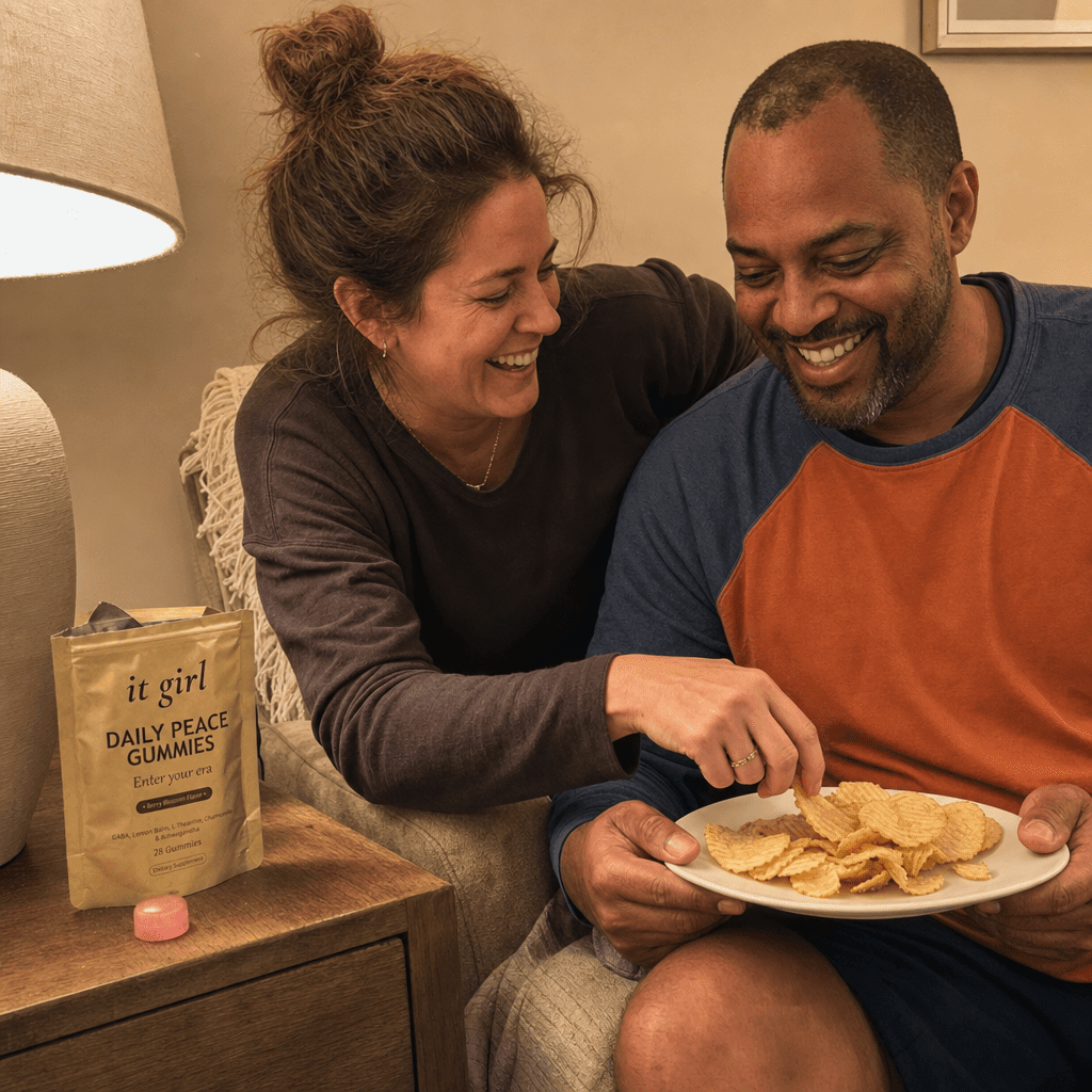 Reconnected mom on the couch stealing a chip off her husband's plate, both laughing, the real gold It Girl Daily Peace pouch resting on the side table, the lights back on