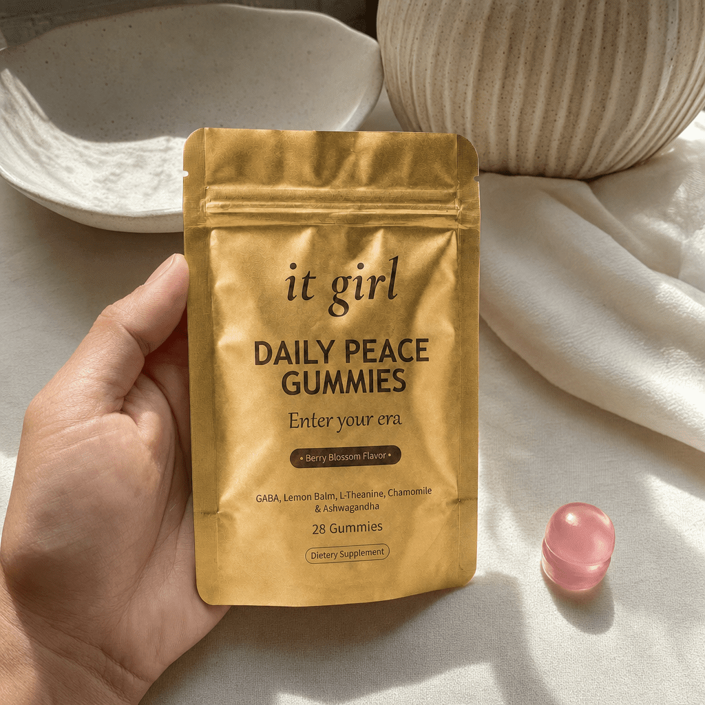 The real matte-gold It Girl Daily Peace pouch in warm daylight on a cream surface beside a single pink gummy, the thing built to rebuild the buffer rather than numb it