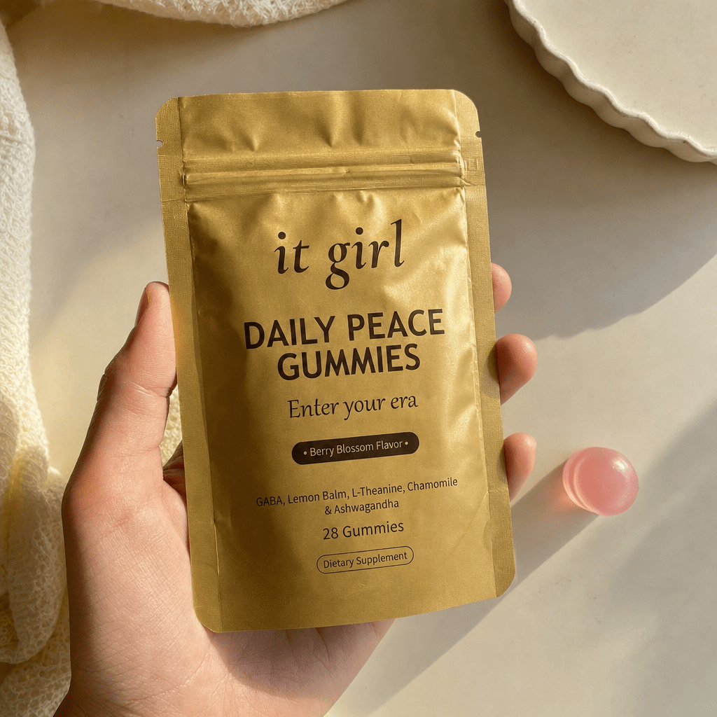 The real matte-gold It Girl Daily Peace pouch in warm daylight on a cream surface beside a single pink gummy, the thing built to rebuild the buffer rather than numb it