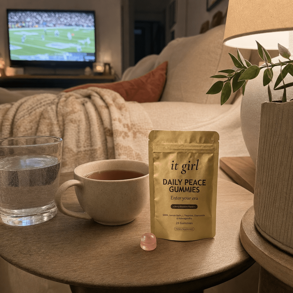 Quiet early-evening living room with the game softly on the TV, a warm cup of tea and the gold Daily Peace pouch on the side table, the calm of an evening that is finally hers, no people
