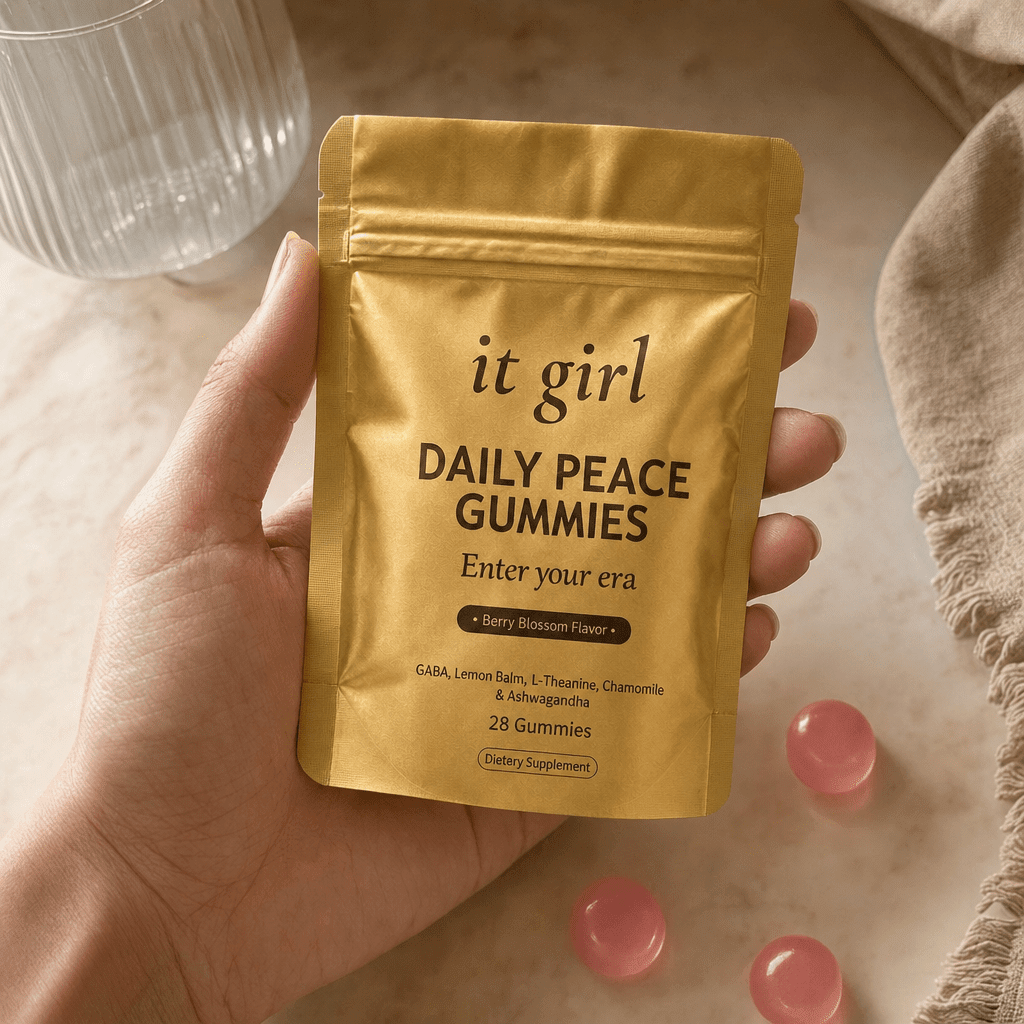 The real It Girl Daily Peace pouch held at palm scale with a few pink gummies and a glass of water in soft daylight
