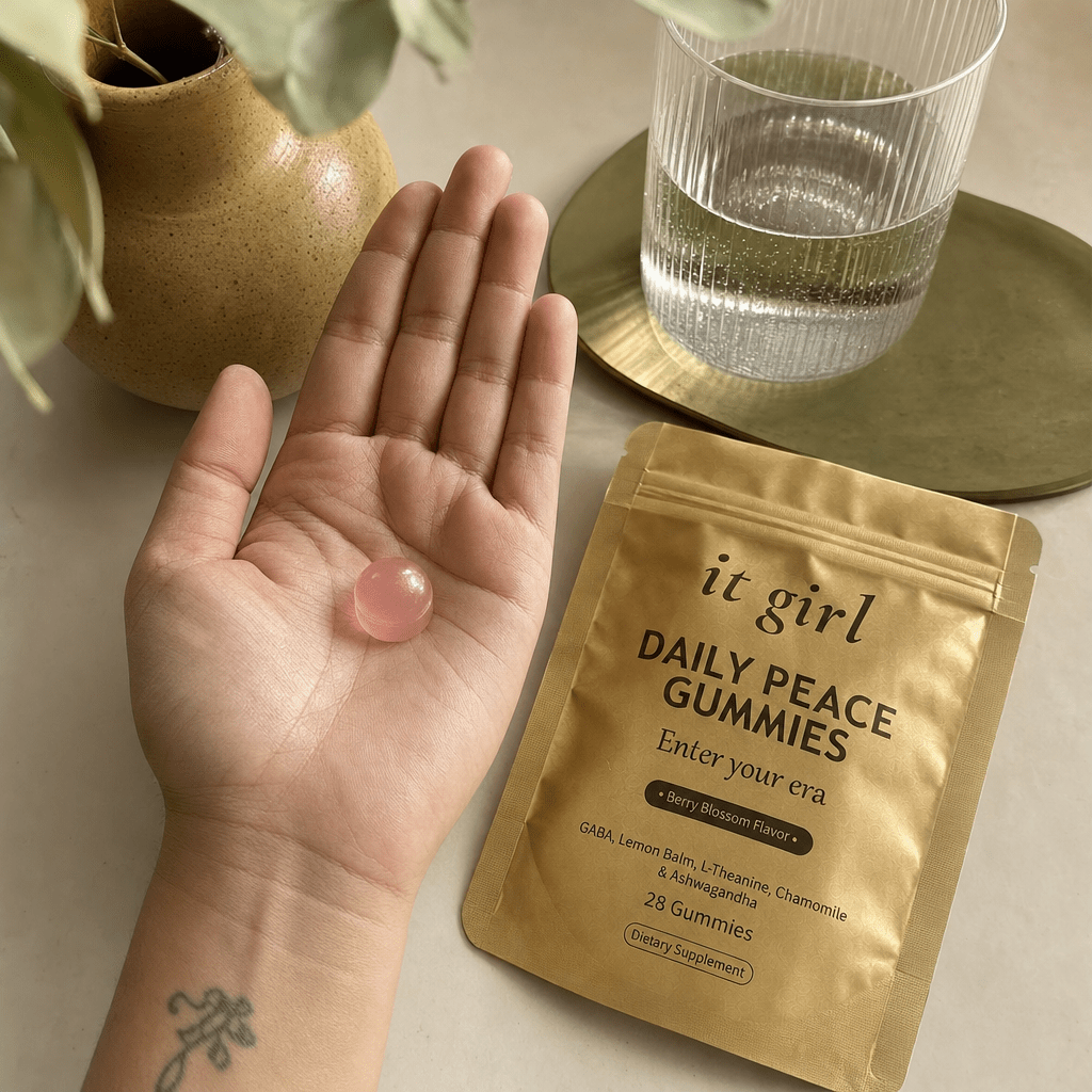 Open palm holding a single pink Daily Peace gummy beside the gold pouch and a glass of water on a cream counter, the GABA and L-Theanine calm signal handed back