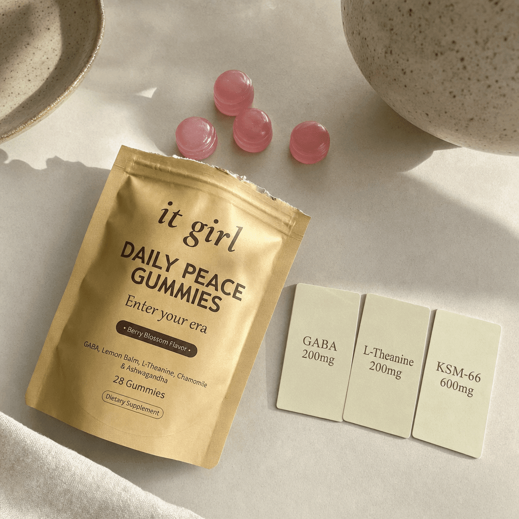 The palm-sized gold It Girl Daily Peace pouch opened at the top beside three dose cards reading GABA 200mg, L-Theanine 200mg, and KSM-66 600mg with a few berry gummies on cream