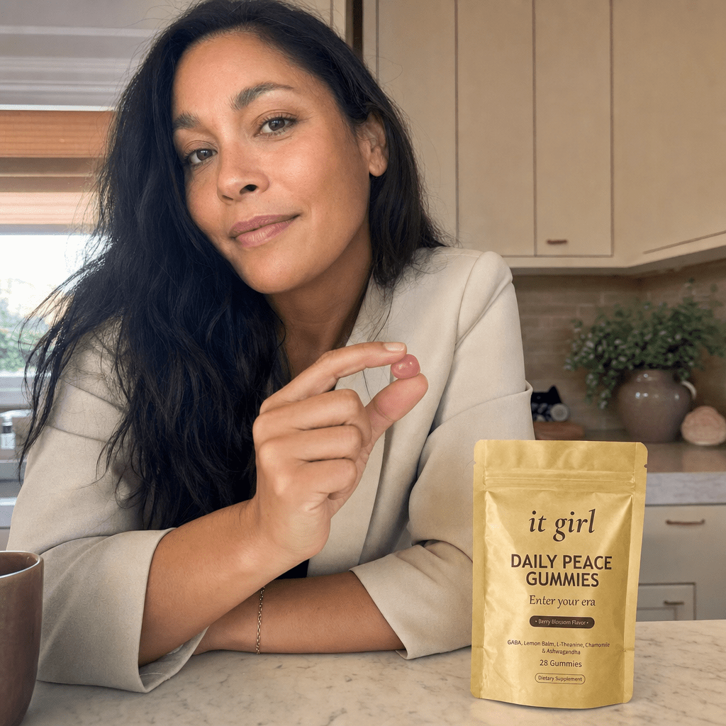 A calm put-together woman in her forties at her morning kitchen counter holding a single gummy with the gold Daily Peace pouch beside her