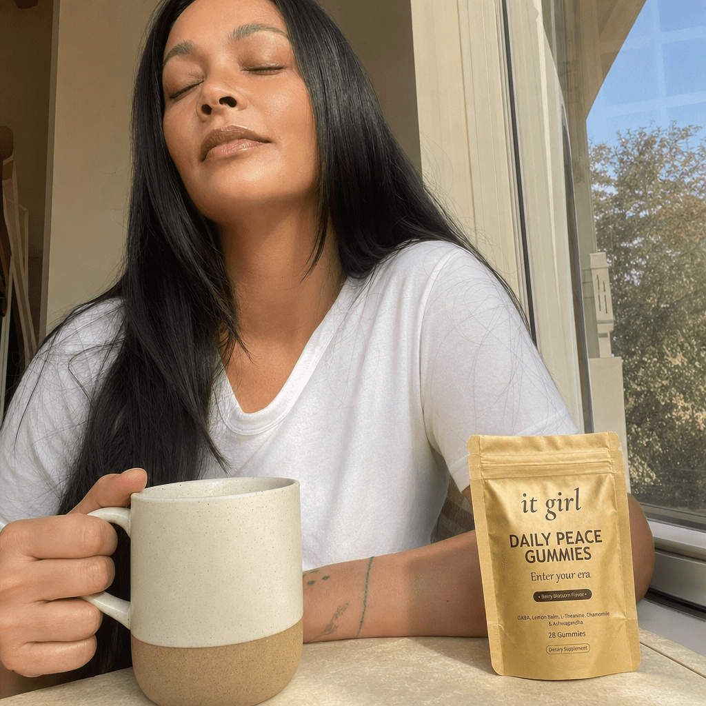 The same woman in her quiet five-minute calm moment by a sunny window with a mug of tea, shoulders dropping, the It Girl Daily Peace pouch on the table beside her