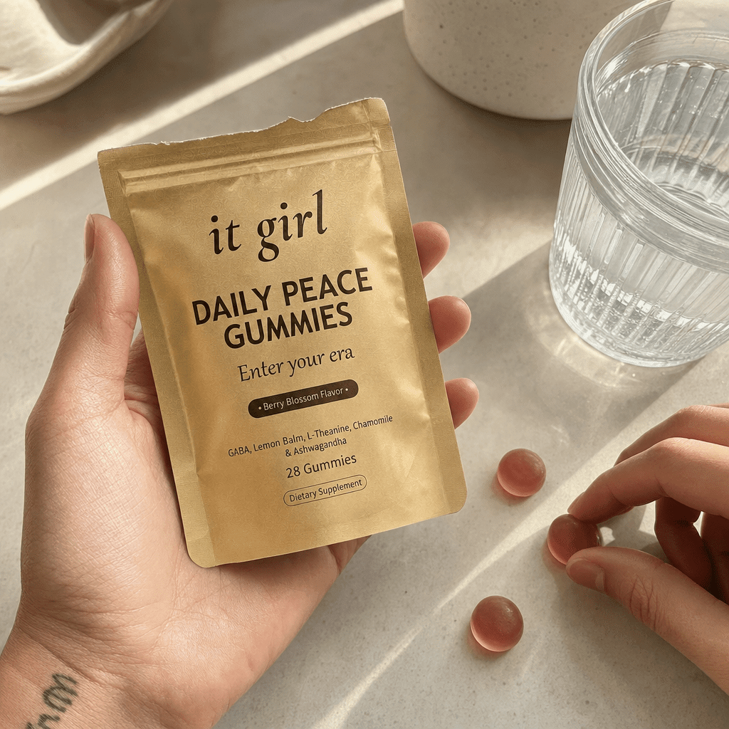 A warm real photo of the It Girl Daily Peace pouch torn open with a few berry-blossom gummies spilled beside a glass of water, the clean calm signal handed over