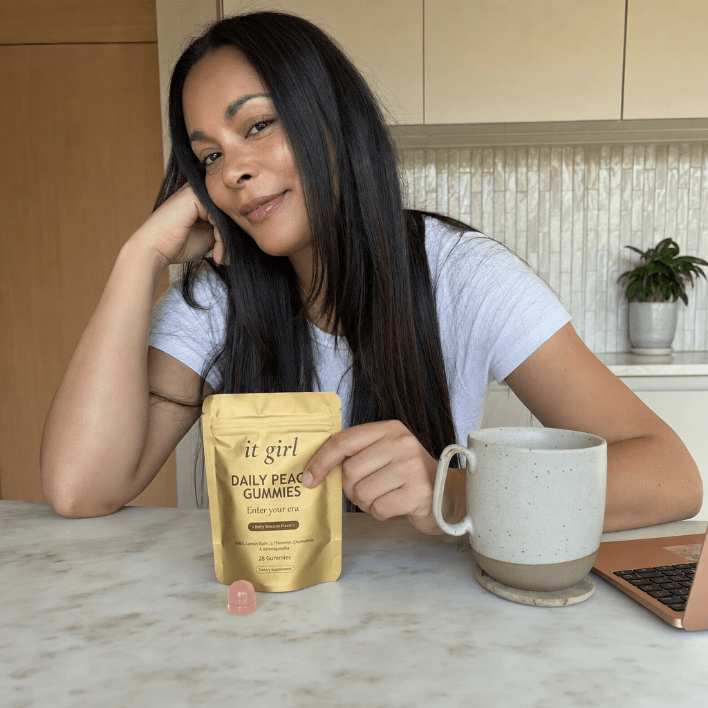 The same woman steadier and calm at her kitchen counter, shoulders relaxed, the It Girl Daily Peace pouch in frame on the counter