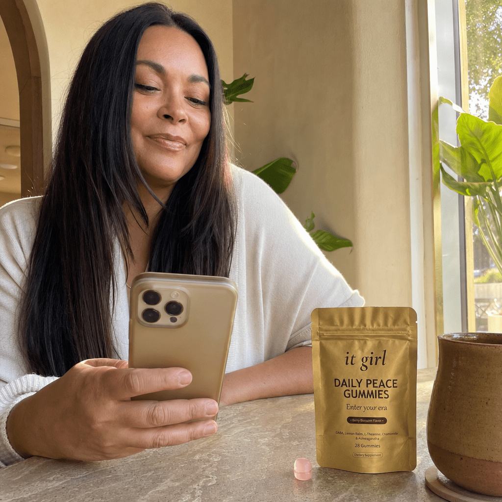 A woman in her forties taking her calm five-minute break with the It Girl app open on her phone and the gold Daily Peace pouch resting beside her