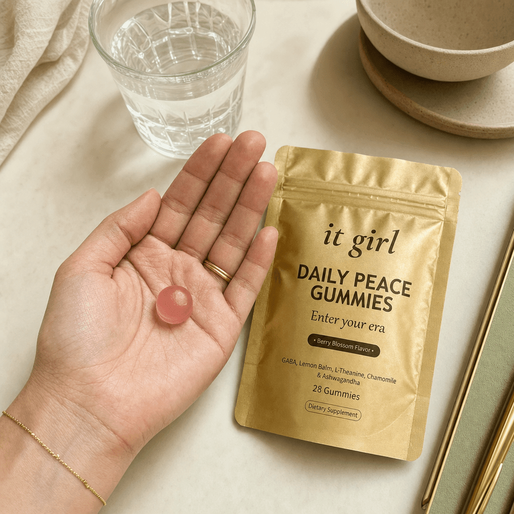 Open palm holding a single pink Daily Peace gummy beside the gold pouch and a glass of water on a cream surface, the GABA and L-Theanine calm signal