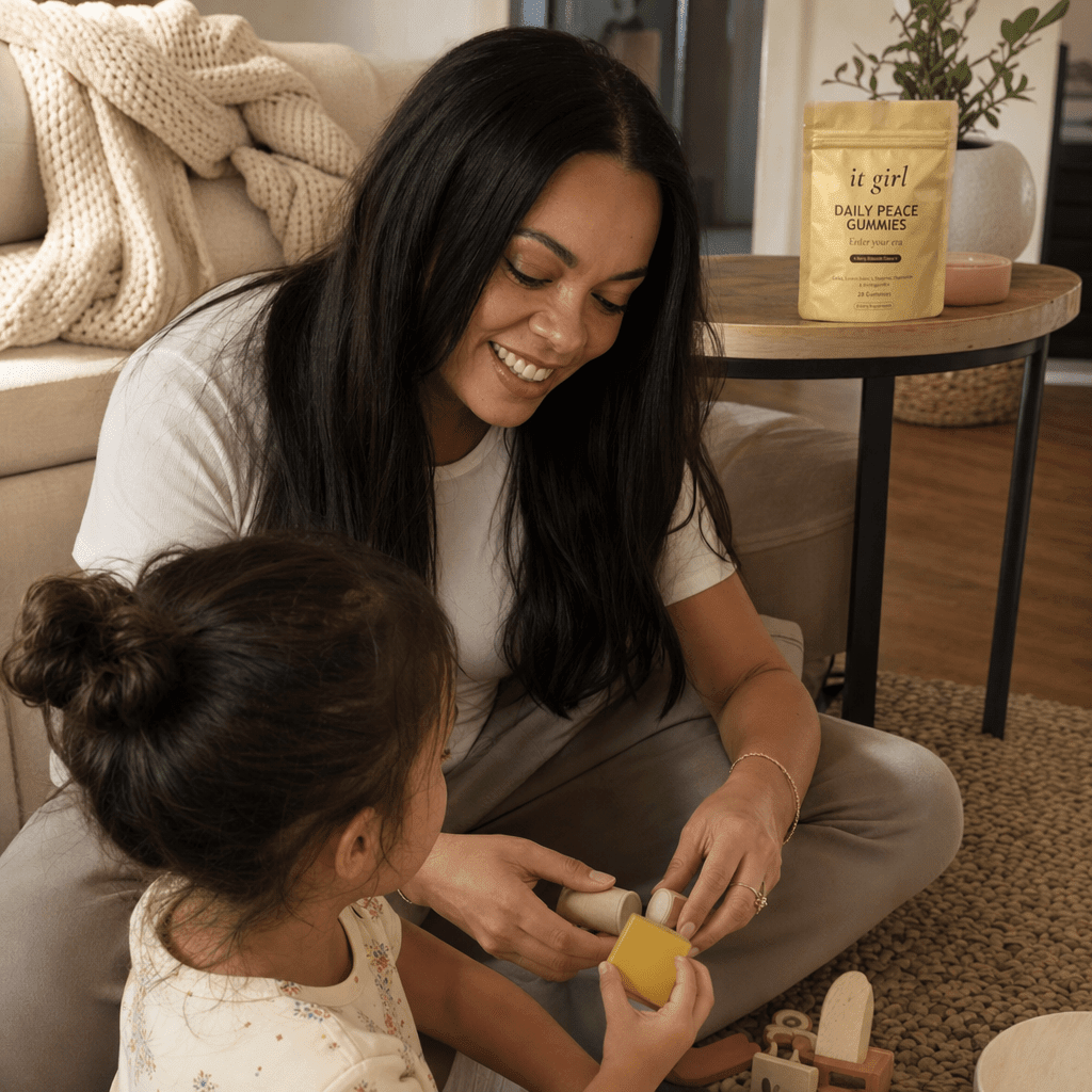 Mom in her forties down on the living-room floor fully present with her young child, relaxed and unhurried, the gold Daily Peace pouch resting on the side table nearby, soft warm light