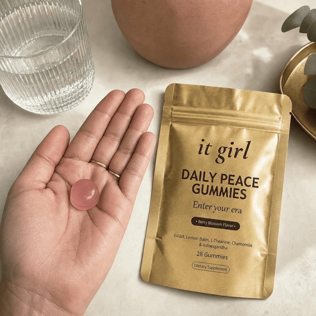 Open palm holding a single pink Daily Peace gummy beside the gold pouch and a glass of water on a cream surface, the GABA and L-Theanine calm signal