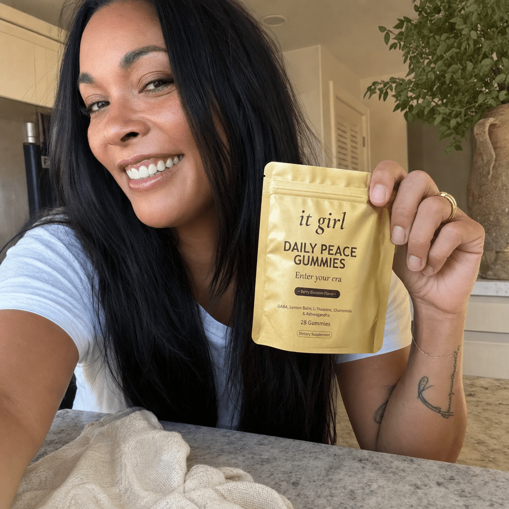 The It Girl Daily Peace pouch on a tidy kitchen counter, a relaxed mom in the warm background