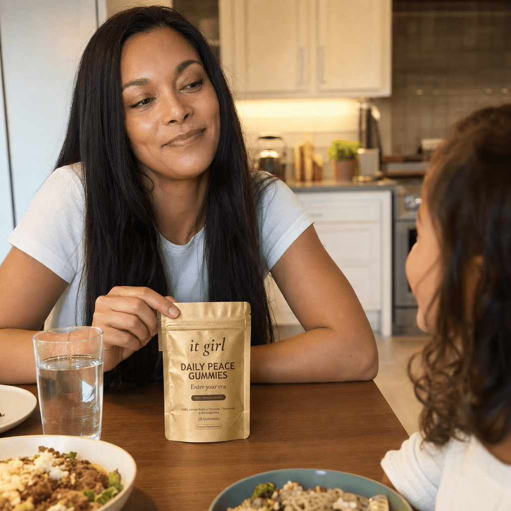Mother in her late forties at the family dinner table, present and relaxed with her child, hand resting easy on the gold Daily Peace pouch on the table while she takes a slow calm exhale instead of stepping outside, soft warm light