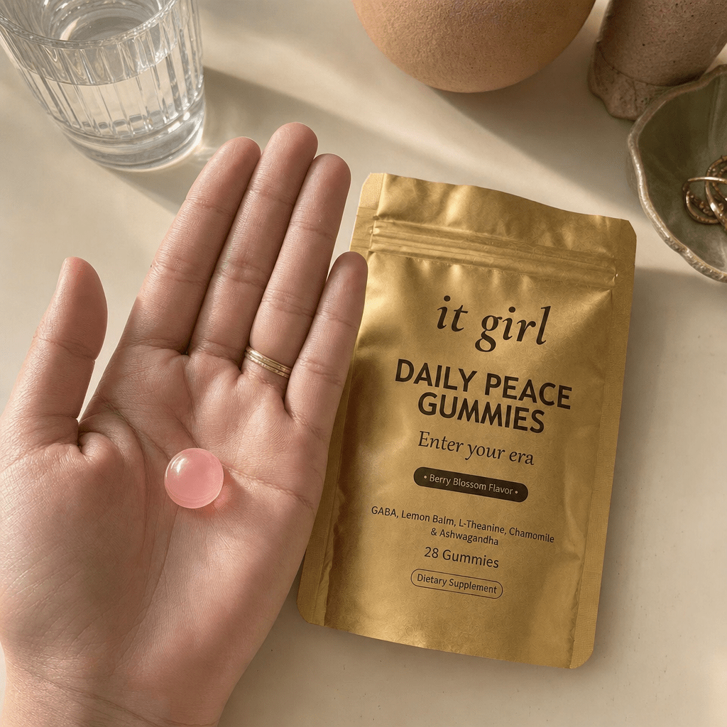 Open palm holding a single pink Daily Peace gummy beside the gold pouch and a glass of water on a cream surface, the GABA and L-Theanine calm signal
