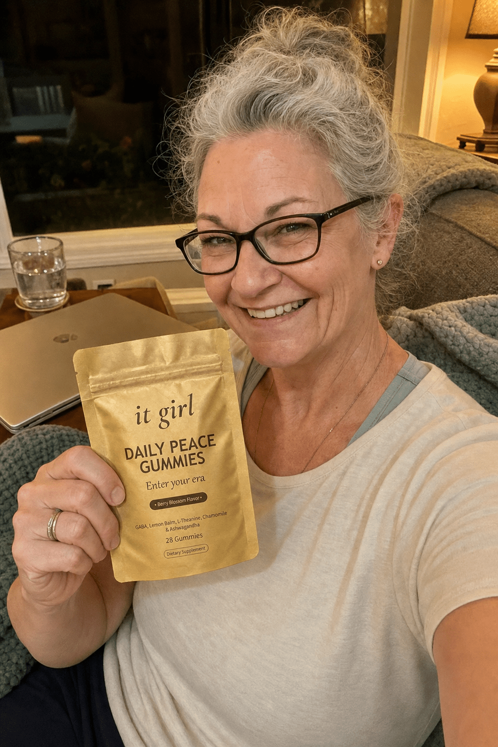 Composed evening couch selfie of a woman about sixty at 7:43, laptop closed, the gold Daily Peace pouch in frame, no wine in sight, the after state