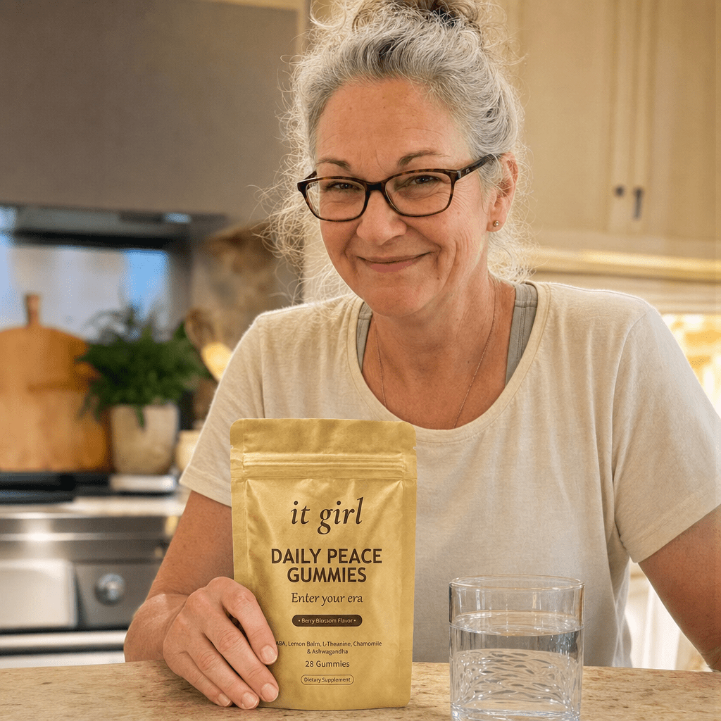 Woman about sixty in her early-evening kitchen, hand resting on the gold Daily Peace pouch, taking a calm exhale instead of reaching for a glass