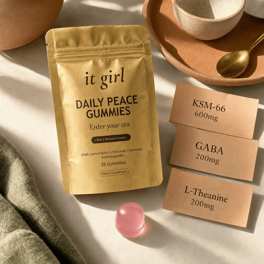 Warm product reveal of the gold It Girl Daily Peace pouch beside a single gummy and three dose cards reading GABA 200mg, L-Theanine 200mg, KSM-66 600mg, the full studied stack