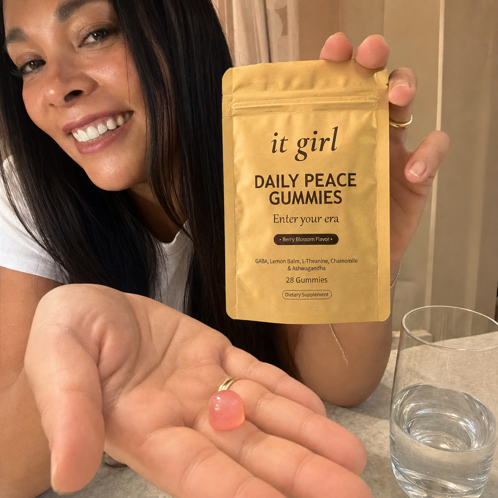 A single pink Daily Peace gummy in an open palm beside the gold pouch and a glass of water on a warm cream counter in early-evening light, calm not sedation, the same evening