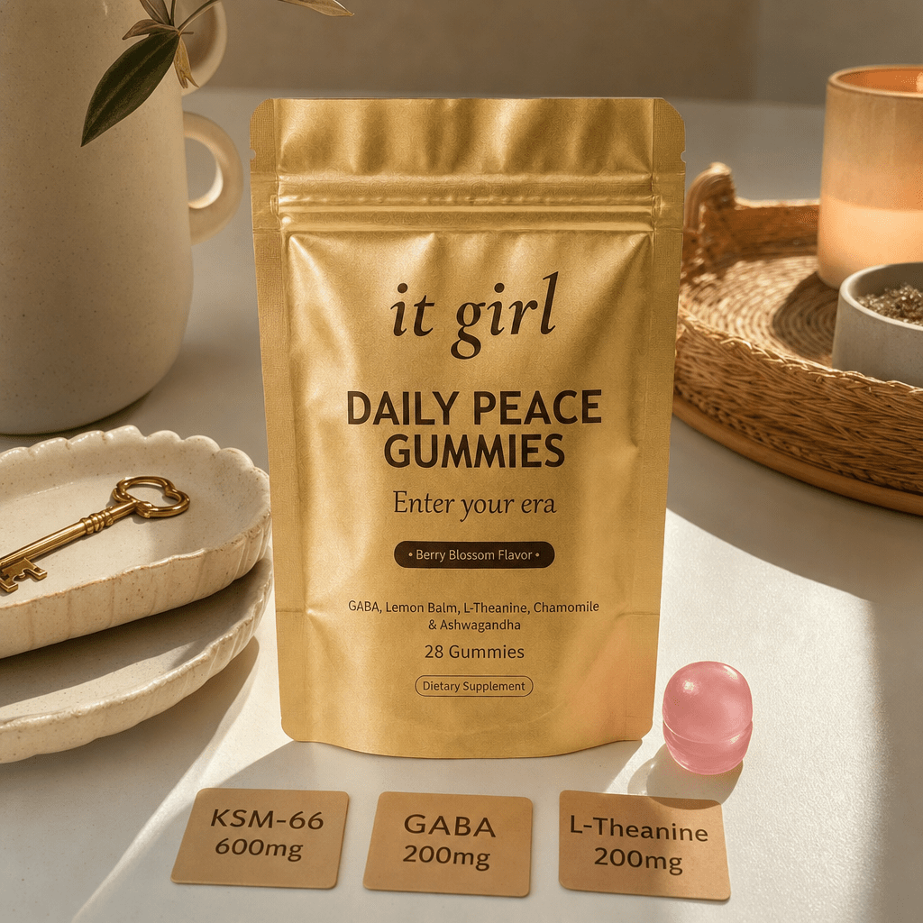 The real matte-gold It Girl Daily Peace pouch with a single pink gummy and three dose cards reading KSM-66 600mg, GABA 200mg, L-Theanine 200mg on a warm cream surface, the clean non-alcohol key