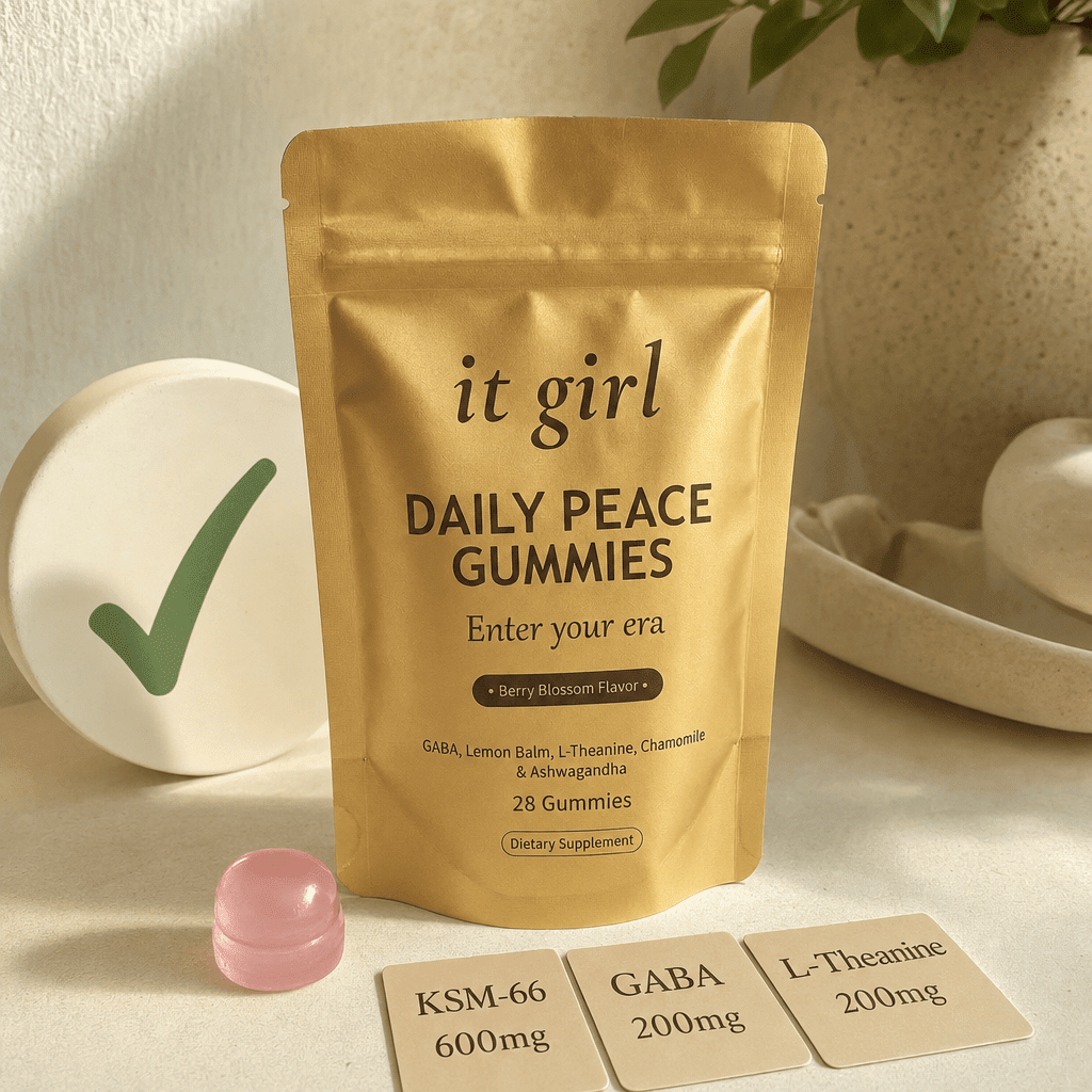 The real matte-gold It Girl Daily Peace pouch with a green checkmark, a single pink gummy, and three dose cards reading KSM-66 600mg, GABA 200mg, L-Theanine 200mg on a warm cream surface, the right vehicle