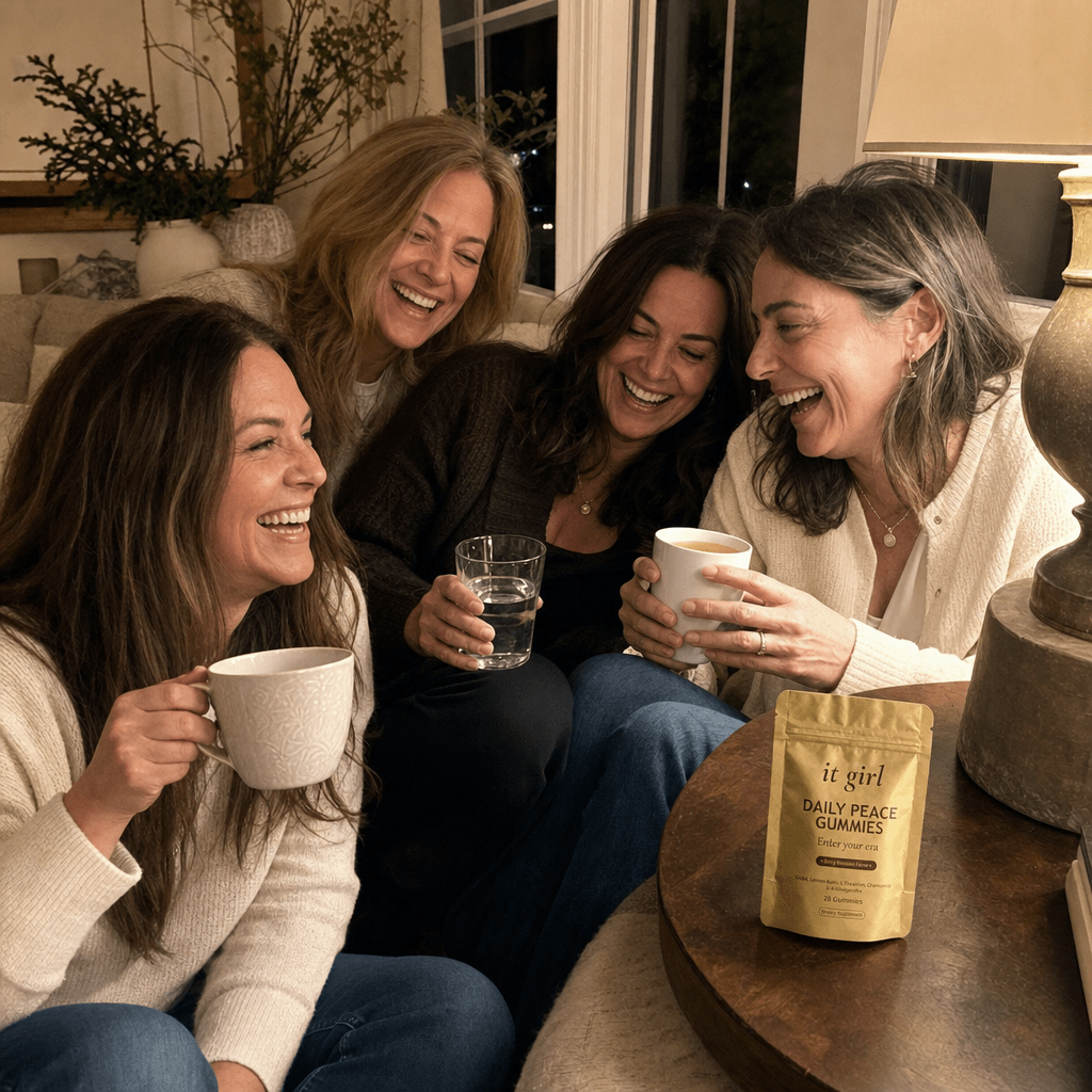 Warm candid group of relaxed women in their forties and fifties laughing together in an evening living room with tea and water, a gold It Girl Daily Peace pouch resting nearby